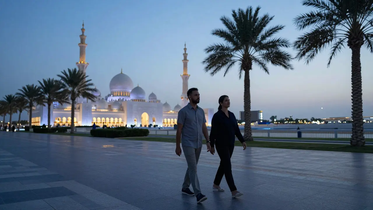 A couple walking along the Corniche at dusk, the Grand Mosque visible in the distance under twilight skies.
